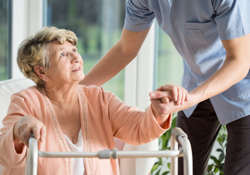 Old woman gets help with walking from a nurse